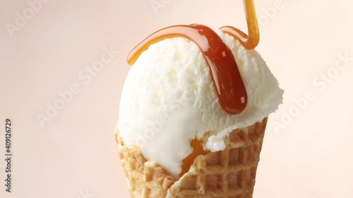 melted caramel sauce flowing on rotating vanilla ice cream in waffle scoop close up photo