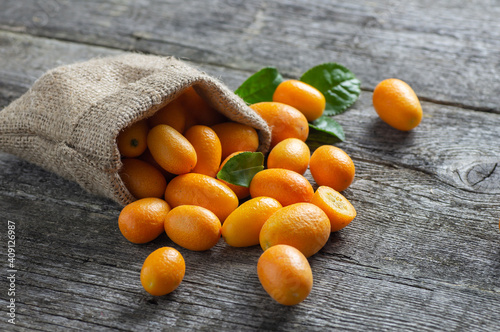Fresh ripe kumquat fruits in burlap sack on wooden background, fortunella margarita