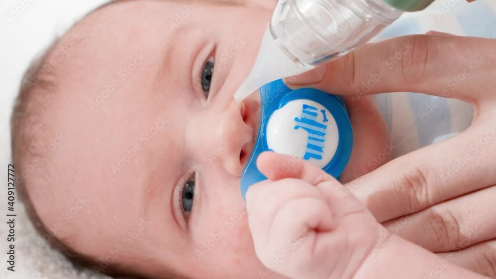 Closeup of little newborn baby lying in crib while mother cleaning his