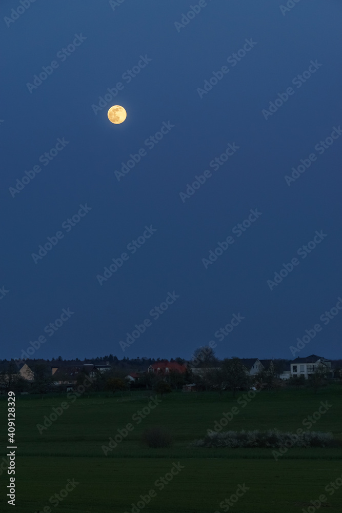 Full moon over rural landscape at blue hour outside village