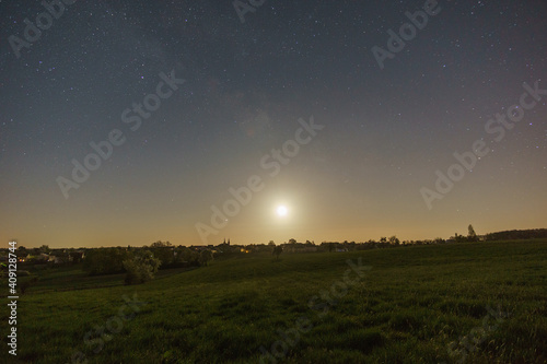 moon and milkyway over meadow with trees outside a german village in the eifel