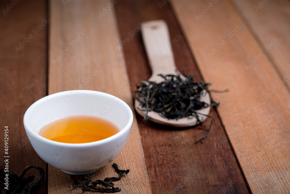 A tea cup with dry tea on the spoon and wooden background A tea cup with dry tea on the spoon and wooden background