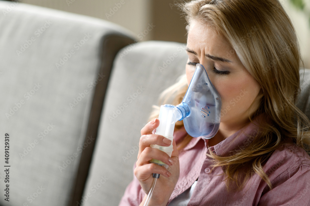 Close-up photo of sick caucasian woman with an inhaler. Unhealthy female doing inhalation at home, she use nebulizer and inhaler for the treatment sitting on the couch at home Close-up photo of sick caucasian woman with an inhaler. Unhealthy female doing inhalation at home, she use nebulizer and inhaler for the treatment sitting on the couch at home