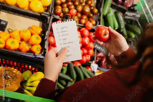 woman follows shopping list when buying fruits and vegetables in supermarket.