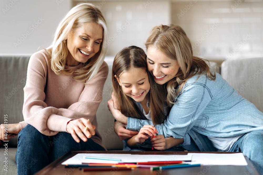 Fototapeta premium Weekend leisure. Cheerful caucasian happy grandmother daughter and granddaughter spend time at home together, drawing with pencils in living room, hugging and laughing