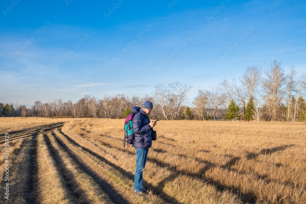 A male tourist with a backpack, with a remote control, controls a drone to take photos and videos of autumn nature.