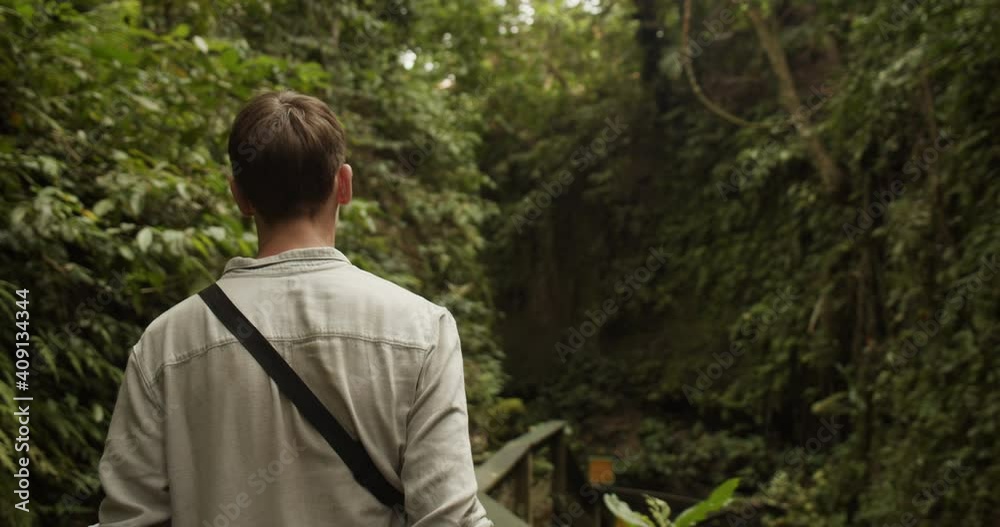 Back view following a young caucasian man exploring a tropical rainforest in Bali Back view following a young caucasian man exploring a tropical rainforest in Bali