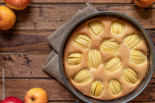 frisch gebackener Kuchen mit eingeschnittenen Äpfeln in Vierteln aus einer Springform zur Jahreszeit Frühling auf einem braunen Tisch aus Holz in der Küche photo