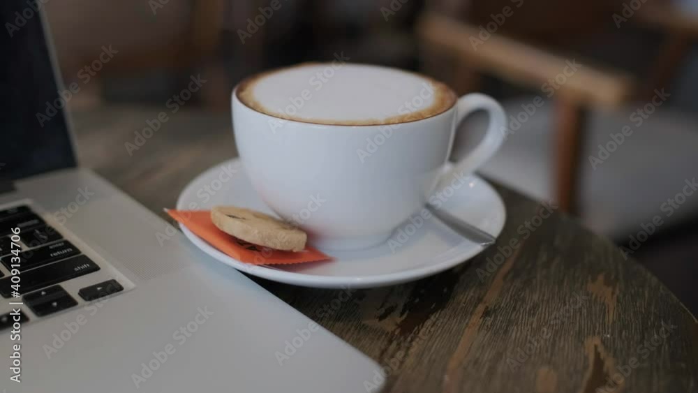 A cup of cappuccino coffee or latte coffee in a white cup with a laptop on the table. Royalty high-quality free stock footage of drink capuccino or latte coffee with a laptop for working in an office A cup of cappuccino coffee or latte coffee in a white cup with a laptop on the table. Royalty high-quality free stock footage of drink capuccino or latte coffee with a laptop for working in an office