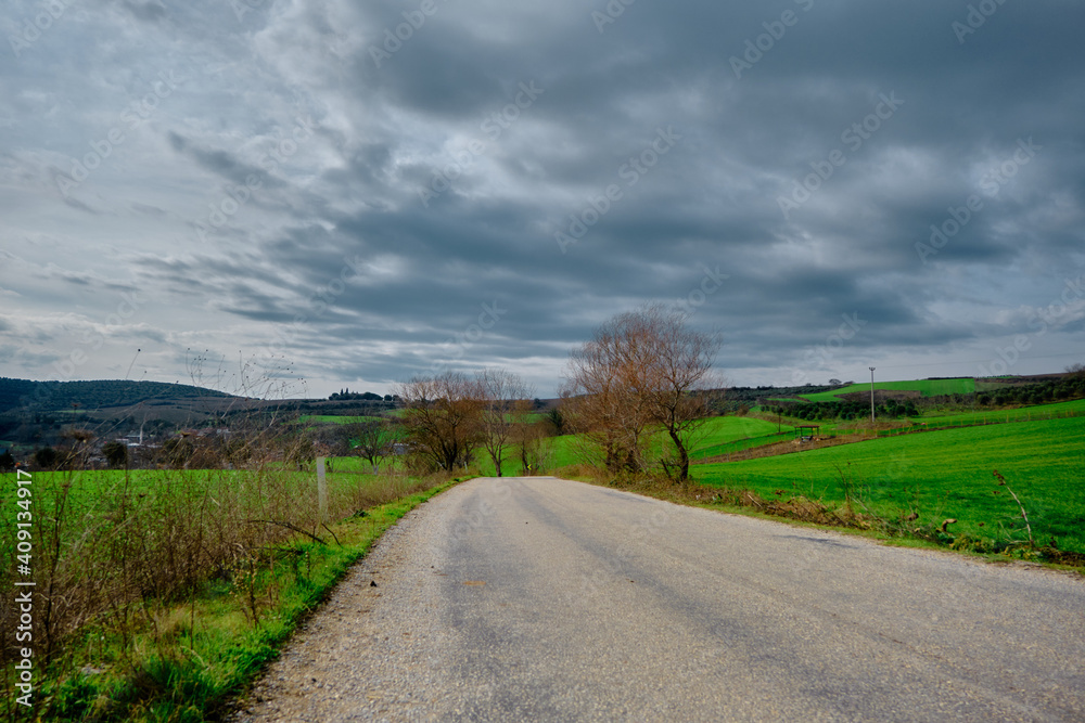 Gravel road and magnificent green grass near the road with cloudy and open sky background. Road sign in next to road.