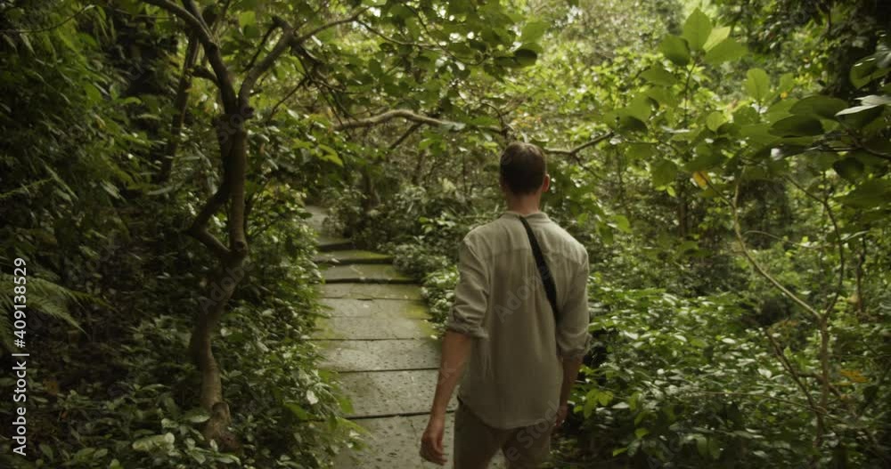 Following handheld shot of a young man walking along the stone path in a tropical rainforest Following handheld shot of a young man walking along the stone path in a tropical rainforest