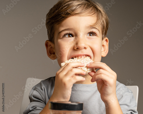 Close up portrait of small caucasian boy four years old eating Crispy puffed rice cake looking to the side - healthy gluten free vegan or vegetarian food - front view studio shot