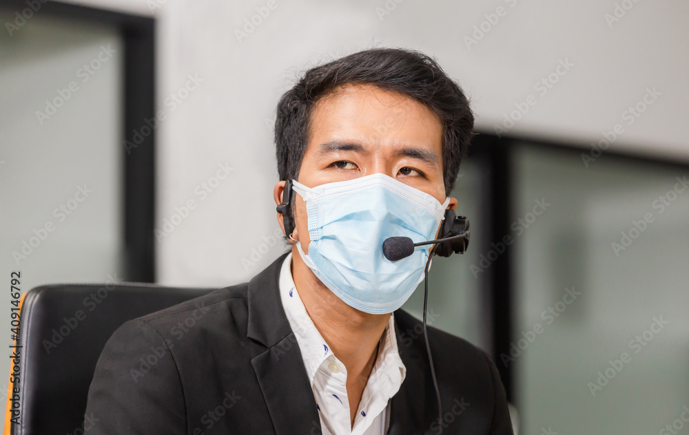 Young asian telephone operator man with headset wear protection face mask against coronavirus, Customer service executive team working at office Young asian telephone operator man with headset wear protection face mask against coronavirus, Customer service executive team working at office