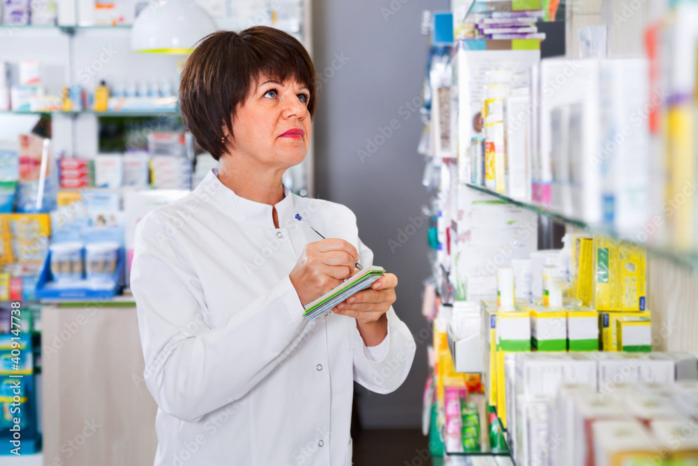 Portrait of cheerful smiling glad female druggist in white coat working in pharmacy
