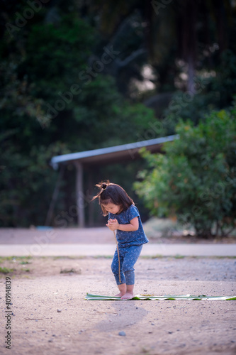 Vertical photo of an Asian girl wearing a blue dress standing to pay homage to the house. Child 3 years old