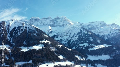 Amazing drone flight of a stunning alpine valley, village and snow covered mountain peaks in Champery, Switzerland. A beautiful winter wonderland scenic flight on a clear blue sky day. photo