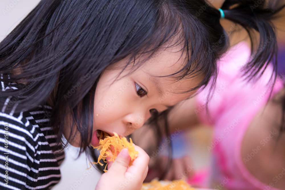 Preschool Asian girl eating Golden thread (Foi thong) for snack during playing in house. Child eat sweet during the day. Dessert increases energy and should be controlled as it may cause obesity. Preschool Asian girl eating Golden thread (Foi thong) for snack during playing in house. Child eat sweet during the day. Dessert increases energy and should be controlled as it may cause obesity.