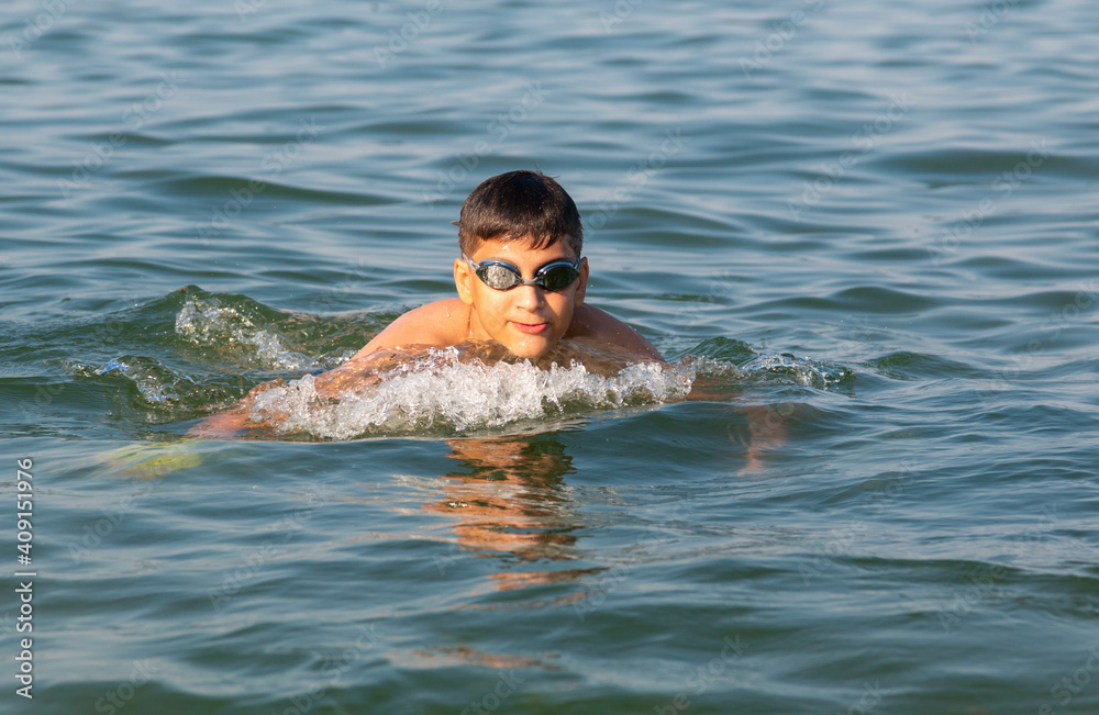 Teenager in goggles swims in the sea with big splashes. Cute boy enjoys swimming in the ocean.  Holidays, vacation with kids