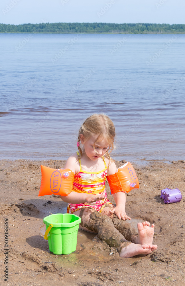 A girl plays on a sandy beach on the shore of a lake in the summer heat. A girl plays on a sandy beach on the shore of a lake in the summer heat.