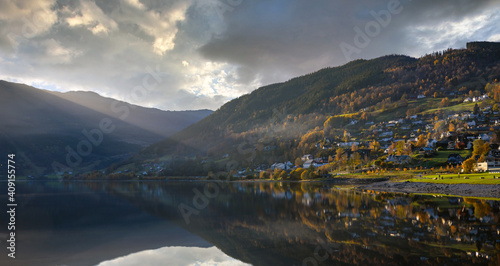 A panoramic view of the lake in Voss Norway, the water is still mirrored and the sun shines down in the evening, the house on the hill with beautiful trees in autumn. photo