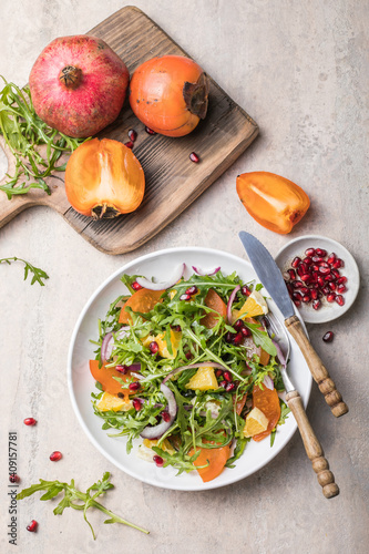 Delicious persimmon salad with arugula  and orange served on light grey table, flat lay. Space for text