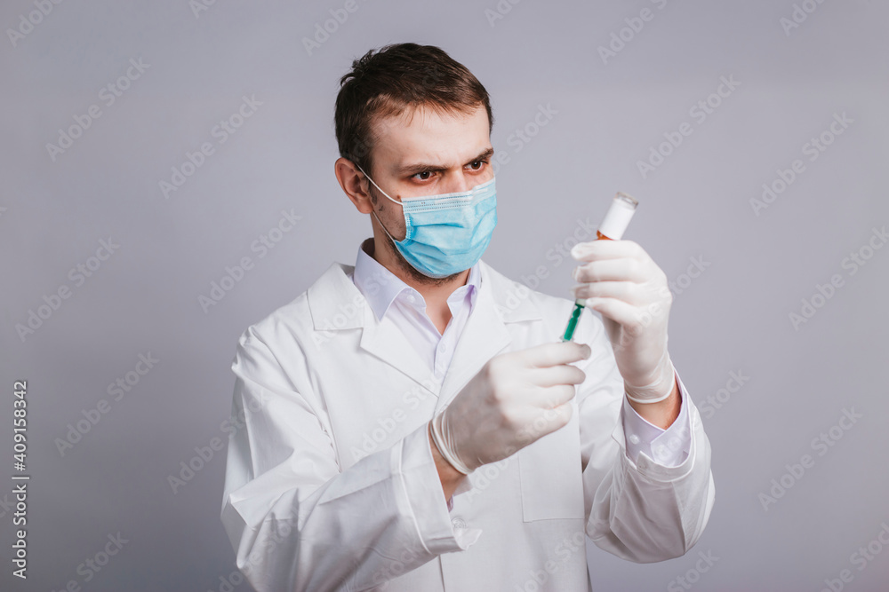 A male doctor in a white coat is taking medicine into a syringe from an ampule. Vaccination and immunization of the population. studio A male doctor in a white coat is taking medicine into a syringe from an ampule. Vaccination and immunization of the population. studio