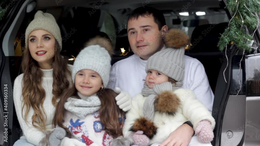 mom dad and two little girls are sitting happily in the trunk of a car hugging each other. Snow forest, family vacation. mom dad and two little girls are sitting happily in the trunk of a car hugging each other. Snow forest, family vacation.