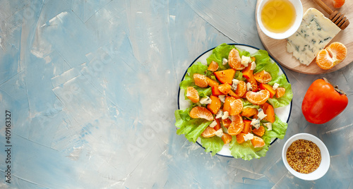 Light sweet and sour salad with persimmon, tangerines and blue cheese. Winter vitamin salad and ingredients on a blue table. Diet food. View from above. Banner. A place for text.