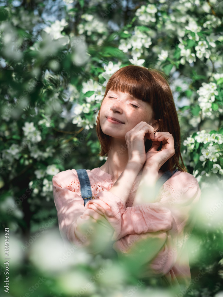 the girl stands in the garden in spring among the flowering apple trees