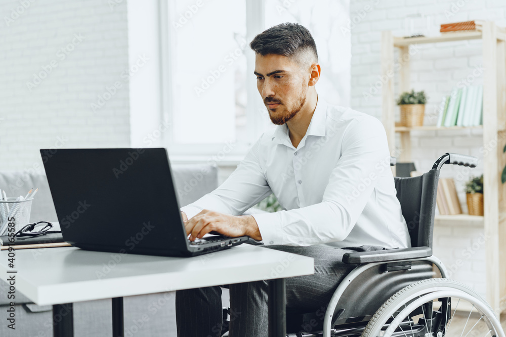Serious concentrated man in wheelchair using his laptop for work / seeking a job in internet Serious concentrated man in wheelchair using his laptop for work / seeking a job in internet