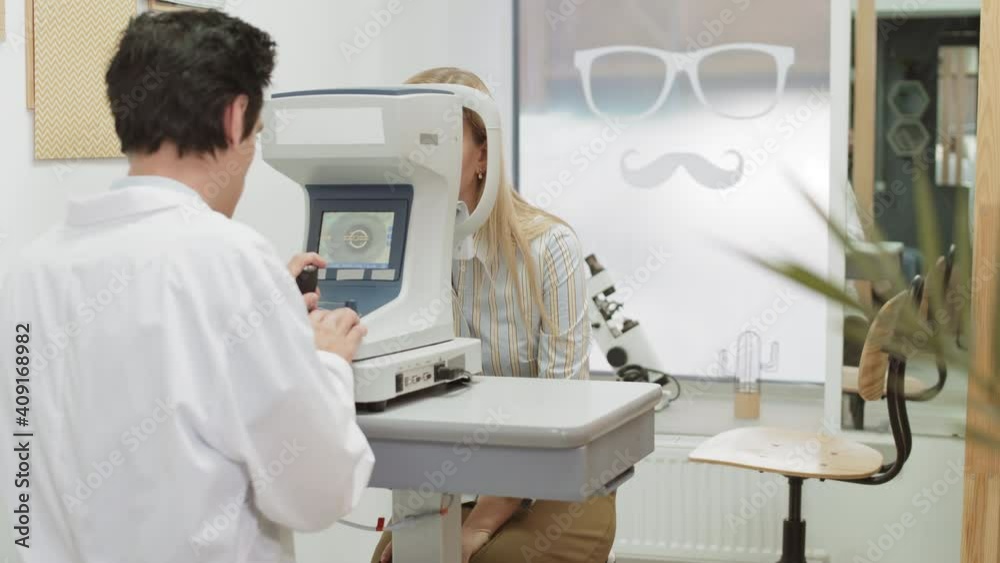 Rear view of Caucasian male ophthalmologist talking to female patient while checking her eyesight using tonometer Rear view of Caucasian male ophthalmologist talking to female patient while checking her eyesight using tonometer