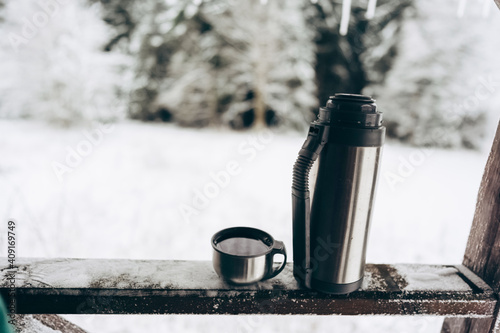 Thermos with hot tea on the veranda of a country house on the background of a beautiful winter landscape.Winter picnic in a snow-covered outdoor park. family holidays during the Christmas holidays