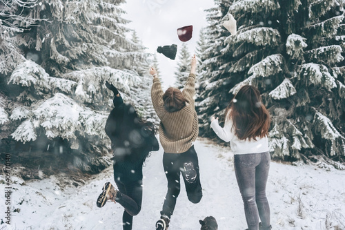 A group of three friends cheerfully jump and throw up their hats against the snow-covered winter landscape.Winter lifestyle.enjoy the little things