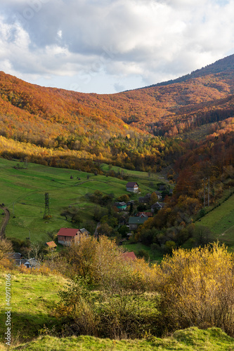 Magnificent panorama of a picturesque mountain village in autumn. Autumn mountain landscape in the Ukrainian Carpathians - yellow and red trees combined with green needles.