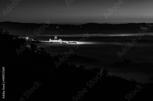 An aerial view of Assisi town and St.Francis church over a sea of fog at night