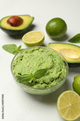 Bowl of guacamole, avocado, lime and basil on white background