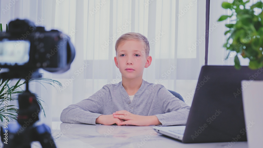 Child blogger videotapes his vlog at home. Boy recording his video blog. White boy speaks in front of a video camera for his blog channel. Little 8 year vlogger makes online streaming using smartphone