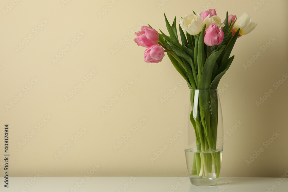 Vase with tulips against beige background, space for text