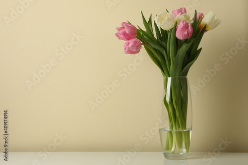 Vase with tulips against beige background, space for text © Atlas