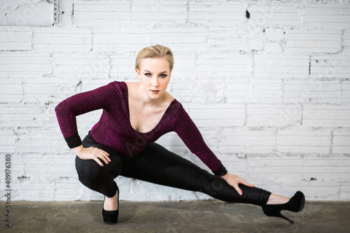 Dancer stretching wearing a purple body suit, black pants, and high heels 