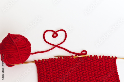 Hand knitting from wool red yarn on white background. The thread is twisted in shape of heart. Handmade gifts and DIY concept for Valentine's Day or mother's day. Close-up view, empty space for text