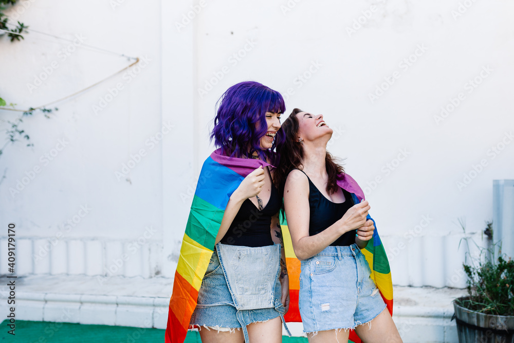 Two women with rainbow flag on a backyard. Couple Young lesbian girls ...