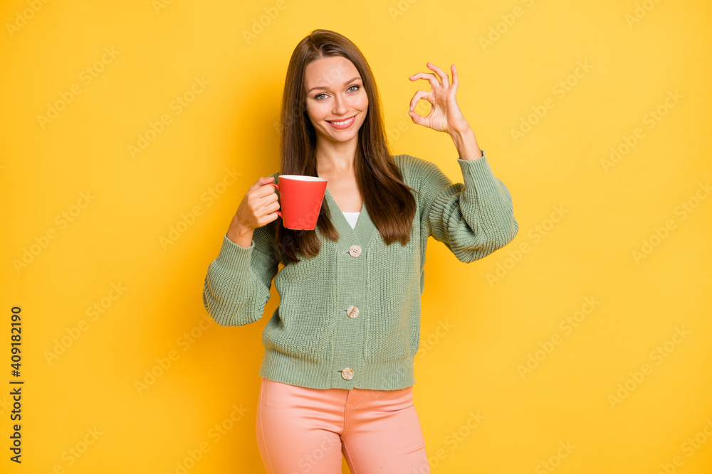 Photo portrait of girl showing ok-sign holding red cup isolated on vivid yellow colored background Photo portrait of girl showing ok-sign holding red cup isolated on vivid yellow colored background