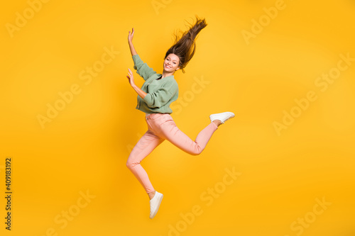 Full size photo of young happy positive good mood cheerful girl jumping with flying hair isolated on yellow color background