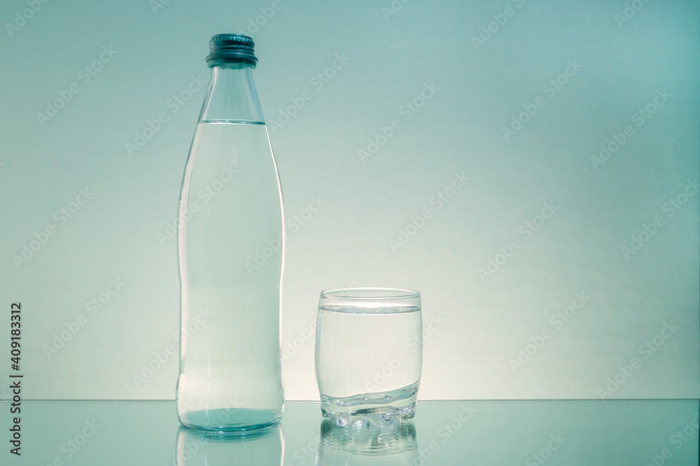 A glass bottle and a glass with clean drinking water are on the table. Copy space. A glass bottle and a glass with clean drinking water are on the table. Copy space.