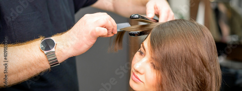 A male hairdresser is straightening the hair of the young woman in a beauty salon