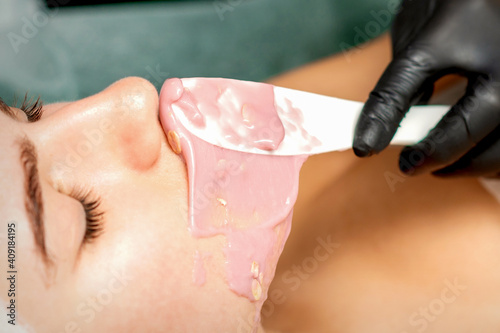 The cosmetologist applying an alginic mask to the face of a young woman in a beauty salon photo