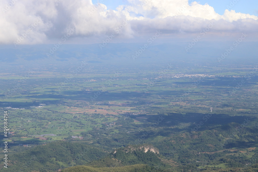 Scenery shot from the top of a high mountain with a cool breeze. Above there were large clouds gathering. Below are many green trees. And there are shadows from the clouds. Take photo in Thailand.