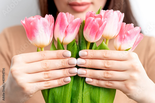A young caucasian woman holds pink tulips in her hands against a white background