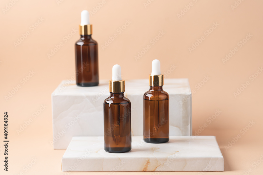 Cosmetic bottles with dark glass pipette on podium of marble boxes. Natural serum concept. Beige background